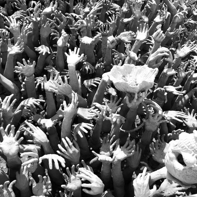 In a monochrome image, numerous outstretched hands reach upwards towards a single large bowl-shaped object. The chaotic scene evokes the urgency and struggle often associated with modern slavery, as hands appear to grasp at the air in desperation.